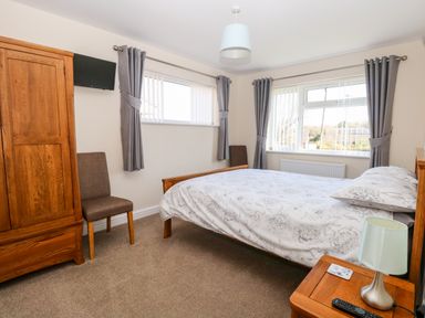 A bedroom with a double bed bedside table lamp wardrobe two chairs and two windows at Elliotts Retreat in Sheringham