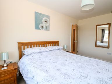 A bedroom with a wooden bed with floral bedding a wooden bedside table with a lamp a mirror on the wall and a door at Elliotts Retreat in Sheringham