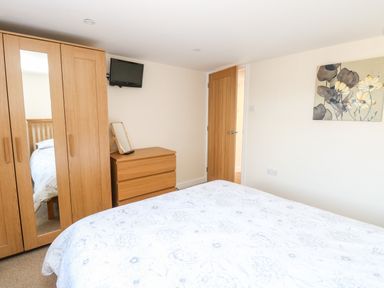 A bedroom with a bed wardrobe a chest of drawers a small wall mounted tv and floral wall art at Elliotts Retreat in Sheringham