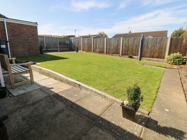 A backyard with a grass lawn wooden bench potted plants and wooden fence at Elliotts Retreat in Sheringham