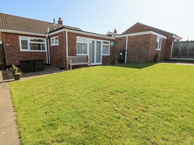 A brick house with white framed windows and doors with a wooden bench and grass lawn at Elliots Retreat in Sheringham