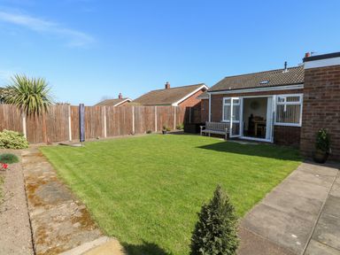 A backyard with green lawn wooden bench and open doors to a brick house at Elliotts Retreat in Sheringham
