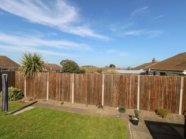 A backyard with a wooden fence grass a paved path and houses in the background at Elliotts Retreat in Sheringham