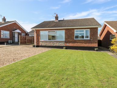 A brick detached house with a lawn and gravel driveway at Elliotts Retreat in Sheringham
