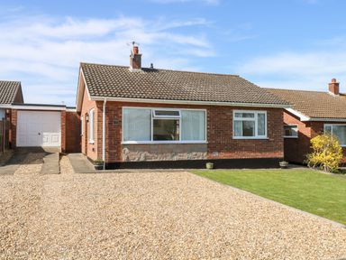 A single-story brick house with a tiled roof a gravel driveway and a small lawn at Elliotts Retreat in Sheringham