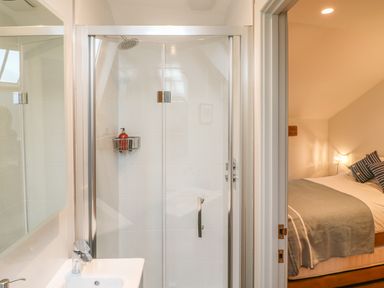A bathroom with a shower enclosure and sink next to a bedroom with a bed and pillows at Lantern Cottage in Padstow