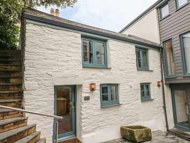 Exterior of a white stone cottage with teal framed windows and door next to stone steps at Lantern Cottage in Padstow