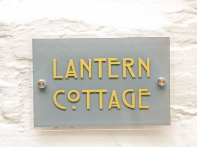 A sign with yellow letters saying Lantern Cottage mounted on a white textured wall at Lantern Cottage in Padstow
