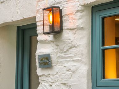 An exterior wall with a lit lantern and a sign reading Lantern Cottage next to blue framed windows at Lantern Cottage in Padstow