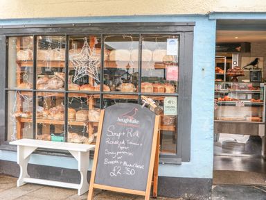 A bakery storefront with shelves of bread visible through windows and a chalkboard sign advertising soup and rolls outside at Lantern Cottage in Padstow