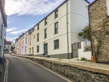 A street with a row of multi-story houses with different colored facades and a stone retaining wall at Lantern Cottage in Padstow