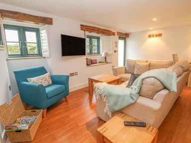 A living room with a beige sofa a blue armchair a wooden coffee table a wall mounted television and windows with shutters at Lantern Cottage in Padstow