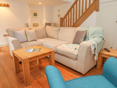 A living room with a beige sectional sofa a wooden coffee table and a blue chair at Lantern Cottage in Padstow