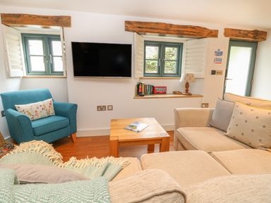 A living room with a beige sofa a blue armchair a wooden coffee table and a wall-mounted TV at Lantern Cottage in Padstow