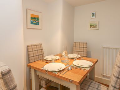 A dining area with a wooden table set for four and plaid upholstered chairs at Lantern Cottage in Padstow