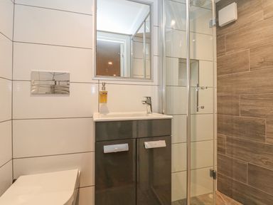 A bathroom with a toilet sink cabinet mirror and glass shower enclosure at Lantern Cottage in Padstow