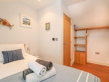 A bedroom with a bed with striped pillow and rolled towels and wooden shelves near a door at Lantern Cottage in Padstow