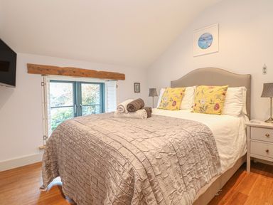 A bedroom with a large bed with yellow floral pillows and rolled towels on the bed at Lantern Cottage in Padstow