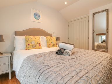 A bedroom with a bed with yellow pillows and folded towels on a gray bedspread with a mirror and closet doors at Lantern Cottage in Padstow