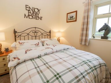 A bedroom with a bed and patterned bedding with bird designs and a plaid duvet at Wagtail Nest Northfield Cottage in Scalby