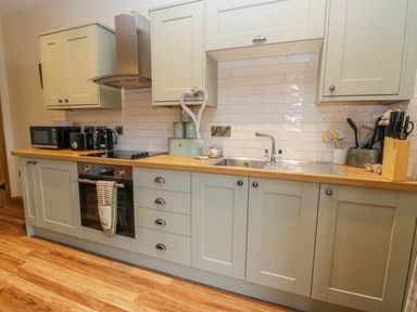 A kitchen with wooden countertop, built-in oven, stove, microwave, kettle, toaster, sink, cabinetry and utensils at Wagtail Nest, Northfield Cottage in Scalby
