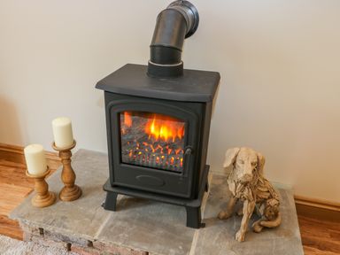 A black wood stove with fire inside next to two white candles on wooden holders and a wooden dog sculpture at Wagtail Nest Northfield Cottage Scalby