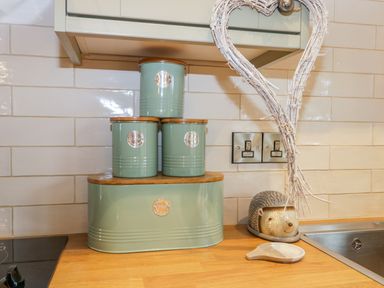 Kitchen countertop with three green canisters stacked on a bread bin beside a heart-shaped decoration and a hedgehog-shaped container at Wagtail Nest Northfield Cottage Scalby