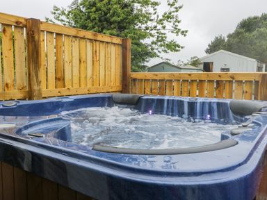 An outdoor blue hot tub with water jets on a wooden deck surrounded by wooden fencing