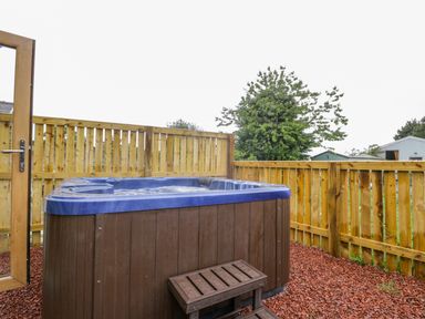 An outdoor hot tub with wooden steps on a small patio enclosed by a wooden fence at Wagtail Nest Northfield Cottage in Scalby
