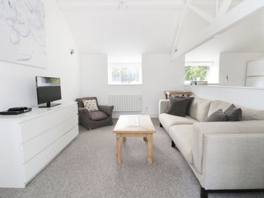 A living room with a beige sofa gray armchair wooden coffee table white dresser and a television at Orchard Cottage in Shaftesbury