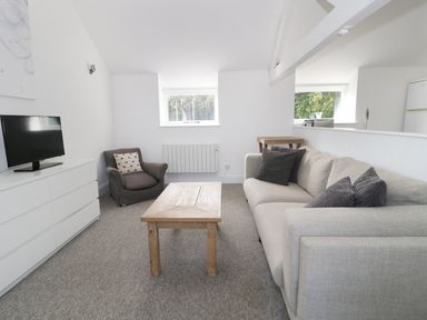A living room with a gray armchair beige sofa wooden coffee table white dresser with television at Orchard Cottage in Shaftesbury
