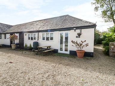 The exterior of a single story cottage with windows a door a picnic bench plant pots and a gravel driveway at Orchard Cottage in Shaftesbury