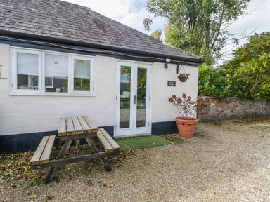 An outdoor area with a wooden picnic table beside a white building with double glass doors and a potted plant at Orchard Cottage in Shaftesbury