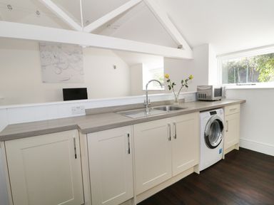 A kitchen with white cabinets a stainless steel sink washing machine microwave and flowers in a vase at Orchard Cottage in Shaftesbury