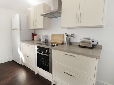 A kitchen with white cabinets a stove a toaster a kettle and a refrigerator at Orchard Cottage in Shaftesbury