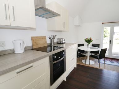 A kitchen with white cabinets a countertop with kettle toaster and utensils and a dining area with a round white table black chairs and flowers at Orchard Cottage in Shaftesbury
