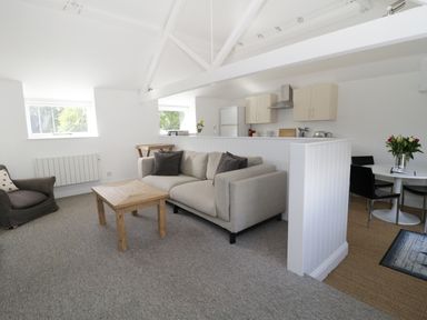 A living room with sofas a wooden table and kitchen area with cabinets and dining table at Orchard Cottage in Shaftesbury