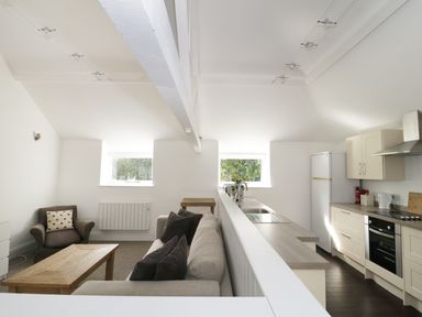 A living area with a sofa an armchair and wooden table next to a kitchen with cabinets and appliances at Orchard Cottage in Shaftesbury
