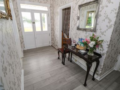 An entryway with a white door a table with flowers and cards a chair and a mirror at Kates Cottage near Ballina County Mayo