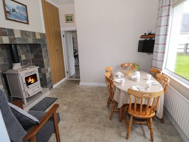 A dining area with a wooden table and chairs set for tea next to a window and a stove with a fire at Kate's Cottage near Ballina County Mayo