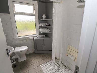 A bathroom with a toilet sink shower with curtain and gray shelving unit holding towels at Kates Cottage near Ballina County Mayo