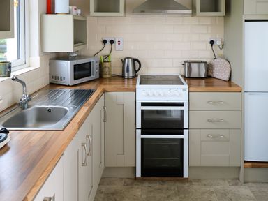 A kitchen with a stainless steel sink microwave oven electric stove kettle toaster and refrigerator at Kates Cottage near Ballina County Mayo