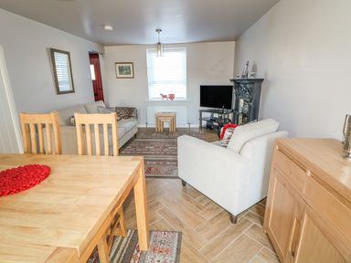 A living room with wooden dining table and chairs a beige sofa armchair fireplace and television at Cranny Corner in Carnlough