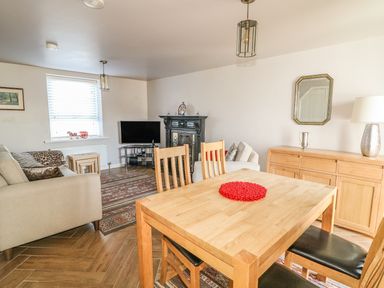 A living room with a wooden dining table and chairs a sofa a television an ornate fireplace a sideboard with a lamp and mirror at Cranny Corner in Carnlough