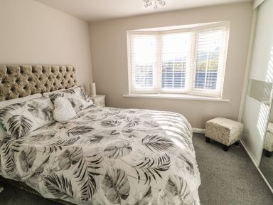 A bedroom with a bed and leaf patterned bedding a bedside table a window with blinds a small upholstered stool and a mirrored wardrobe at Cranny Corner in Carnlough
