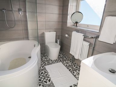 A bathroom with a bathtub a toilet patterned floor tiles and a sink at Cranny Corner in Carnlough