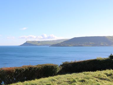 A coastal landscape with a grassy foreground and water leading to hills at Cranny Corner in Carnlough
