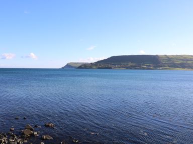 A rocky shoreline with blue sea water and hills in the distance at Cranny Corner Carnlough