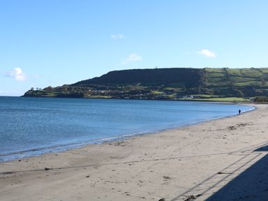 A sandy beach with calm sea water and grassy hills in the background at Cranny Corner in Carnlough