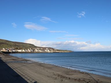 A sandy beach with houses and hills in the background under a blue sky at Cranny Corner in Carnlough